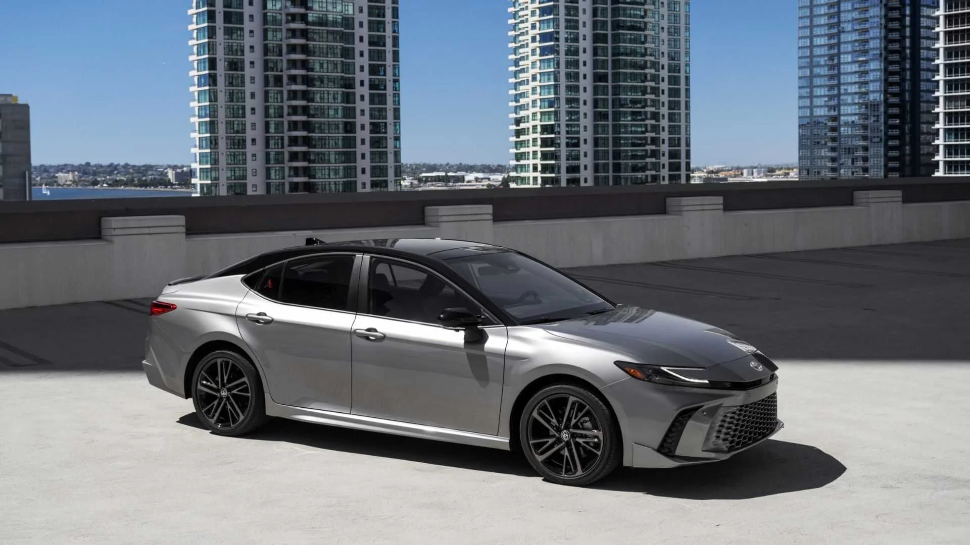 Static side profile shot of a gray 2025 Toyota Camry XSE AWD parked with highrise buildings in the background.
