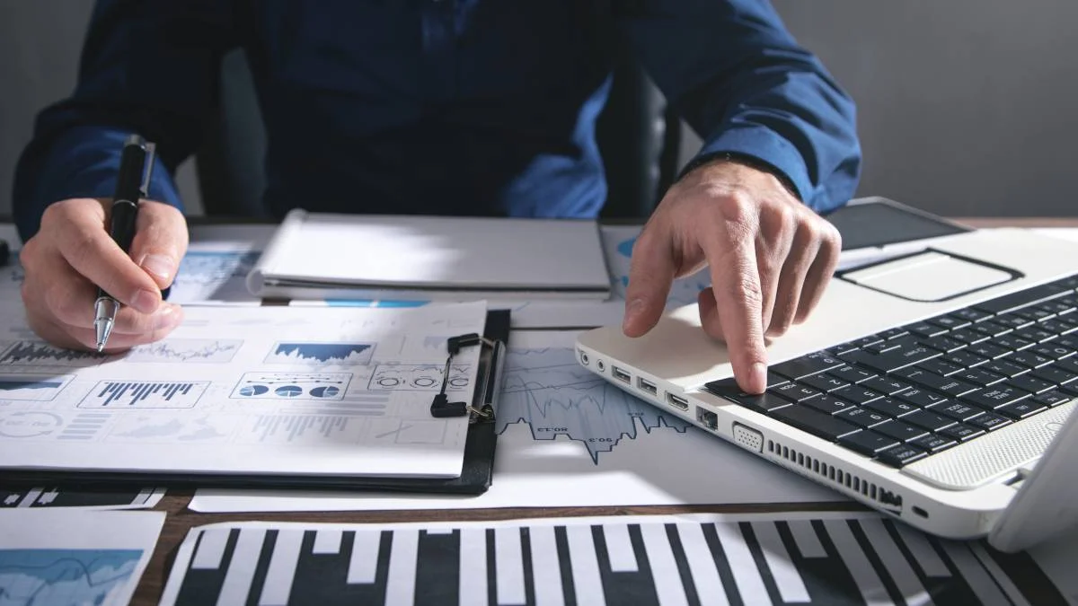 Closeup of financial papers spread out on a desktop next to a laptop.