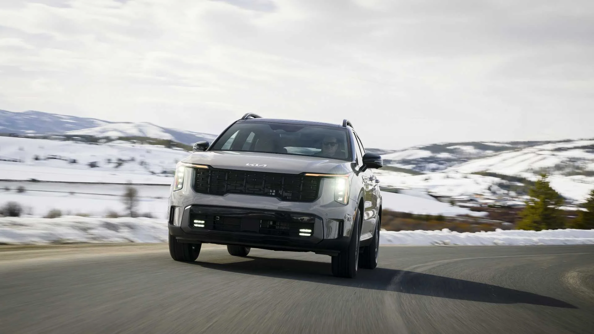 Dynamic front-end shot of a 2026 Kia Sorento driving on a snow-lined country road.