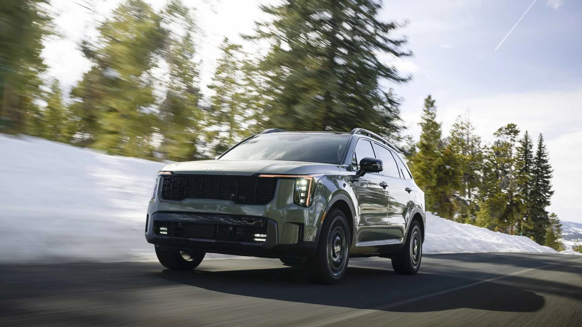 Dynamic front 3/4 shot of a 2026 Kia Sorento driving on a snow-lined country road.