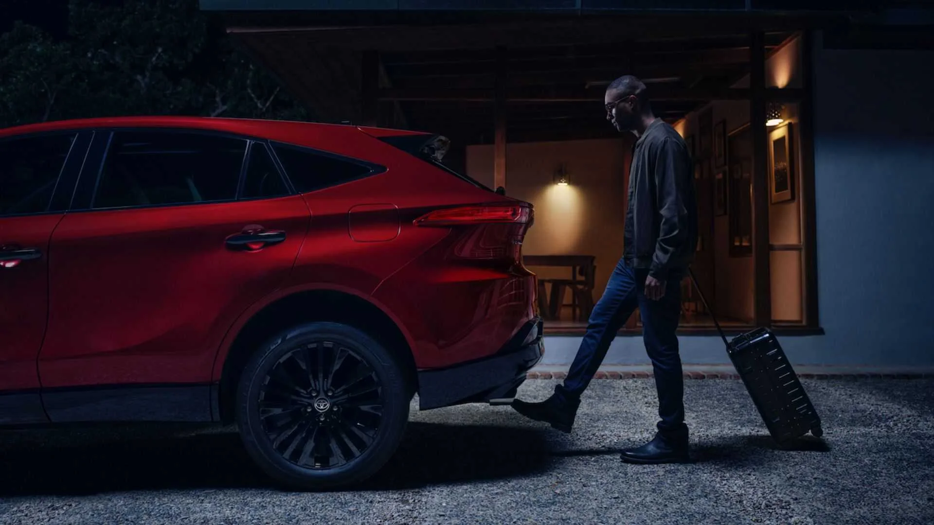 Shot of a man using the tailgate gesture with his foot behind a red 2024 Toyota Venza Nightshade
