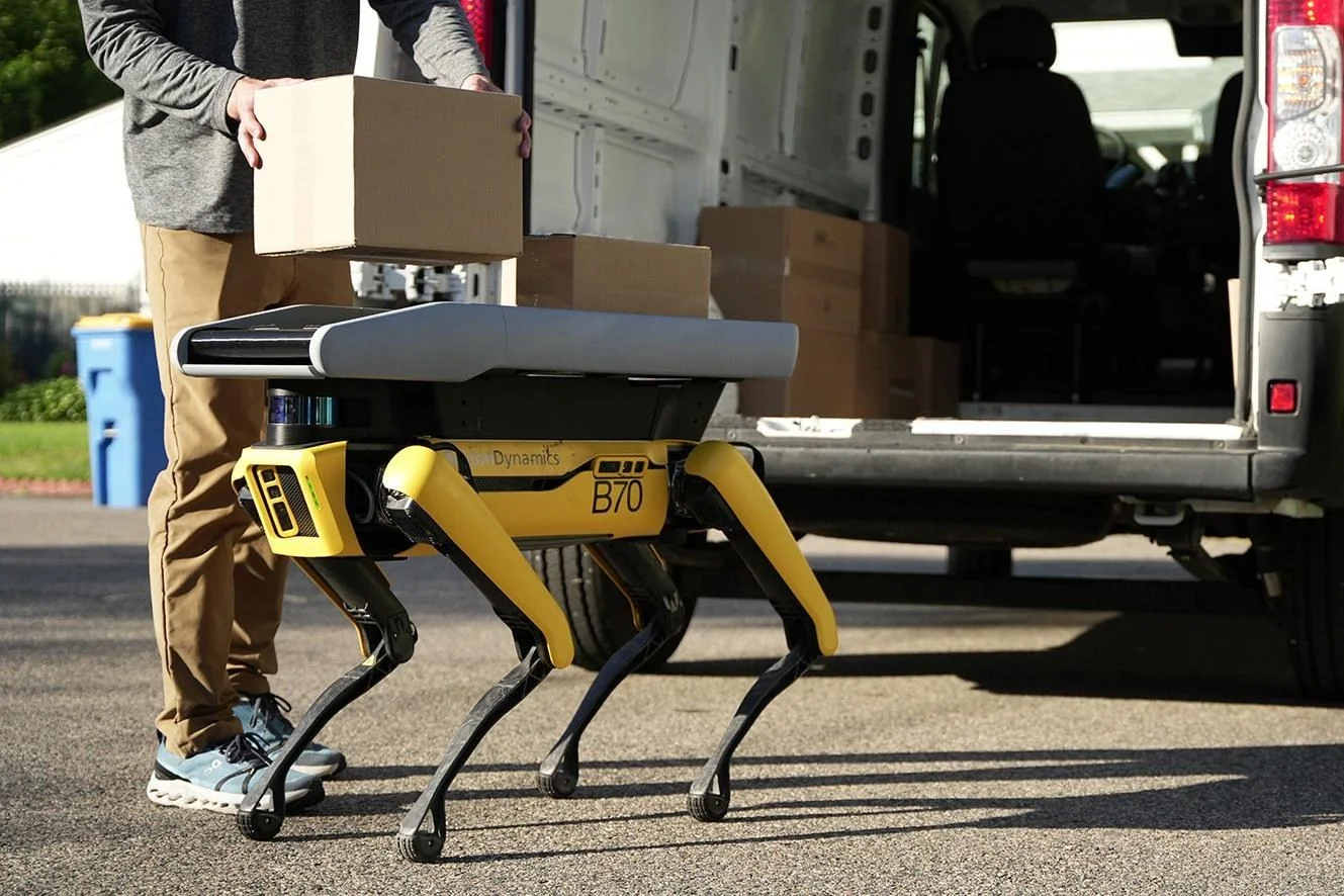 A delivery driver loads cardboard boxes onto Boston Dynamics’ Spot robot from a truck.
