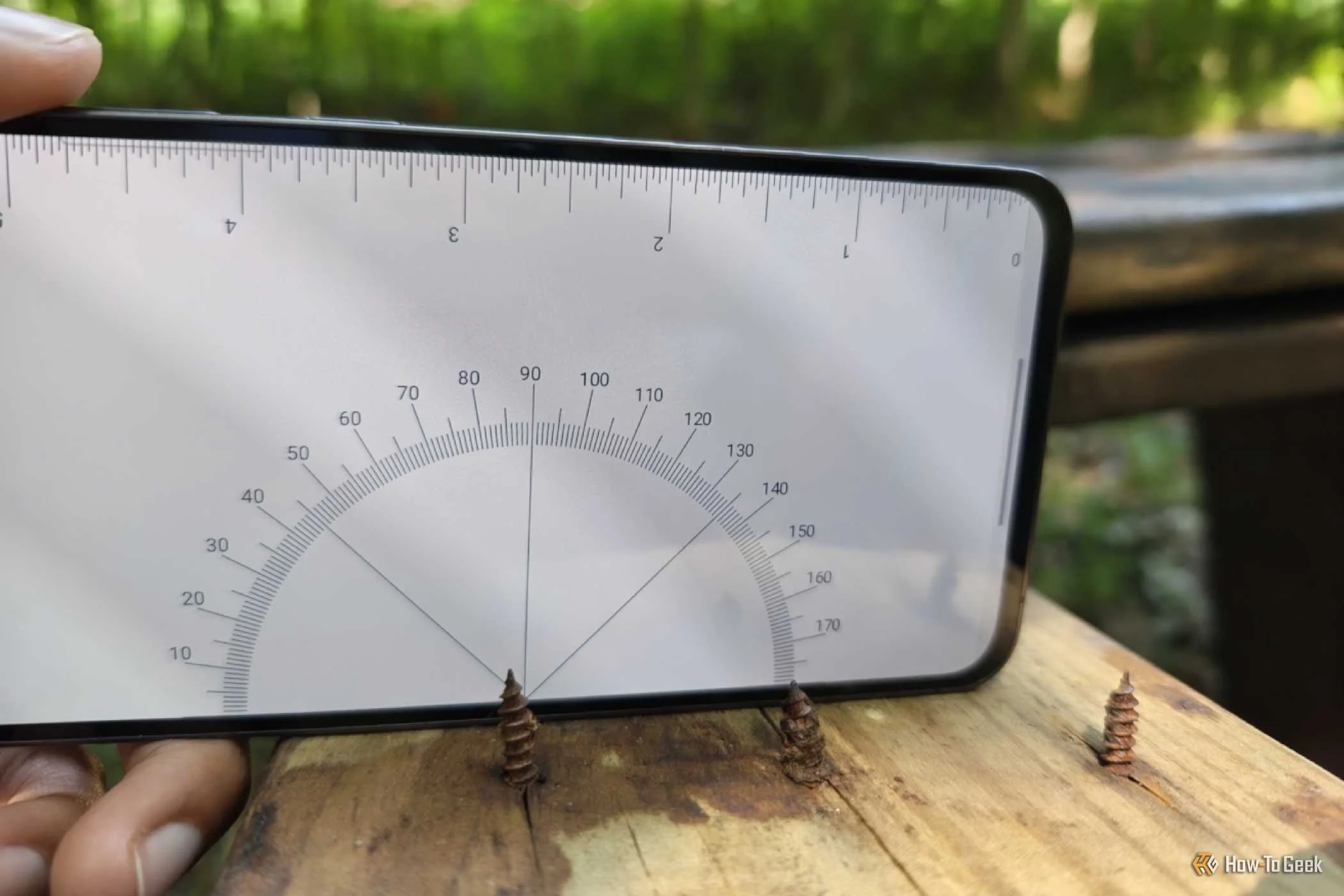A protractor displayed on a Samsung Galaxy phone to measure the angle of a nail sticking out of a wooden bench.