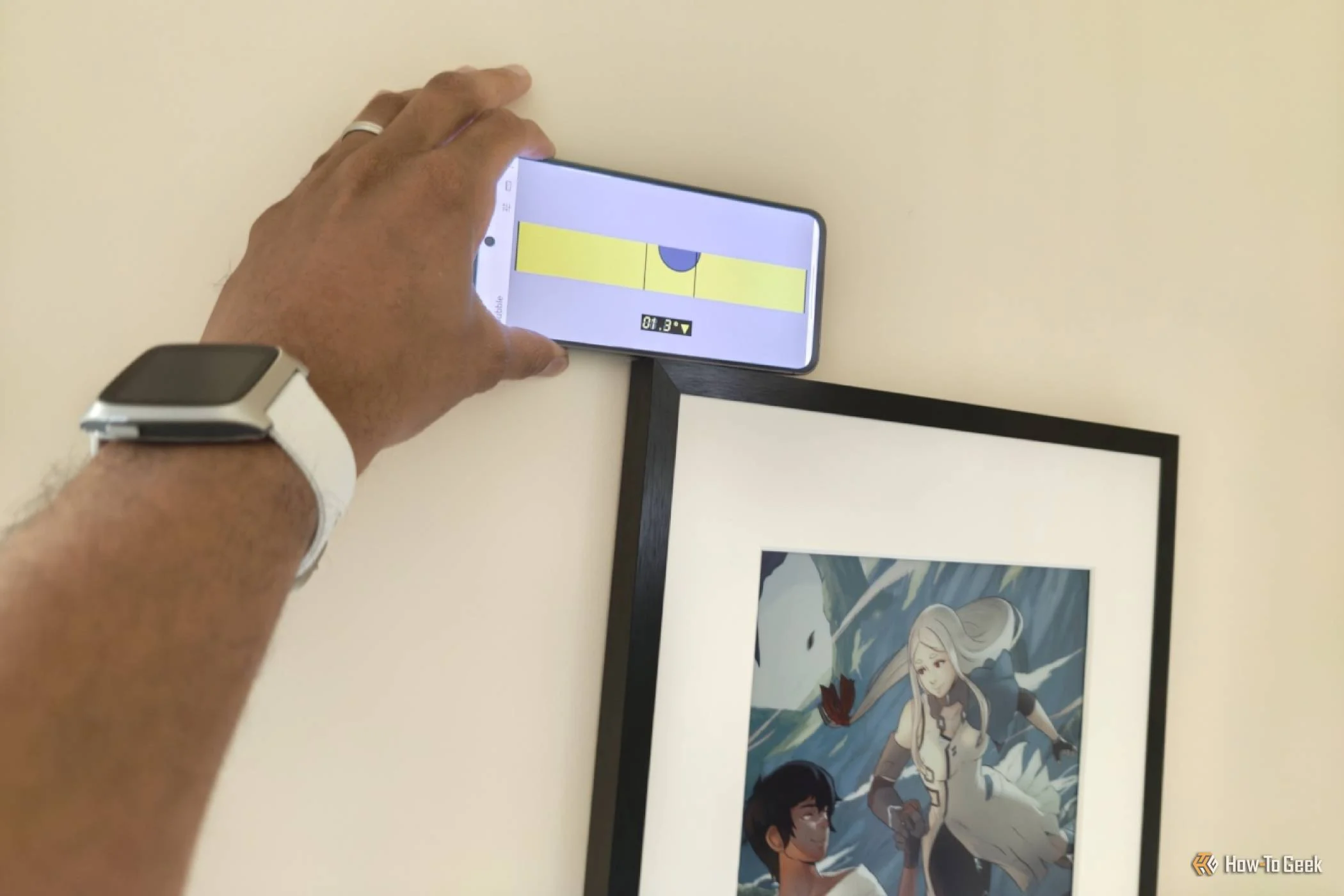 Hand holding a Samsung Galaxy phone displaying a level app to level a picture frame.