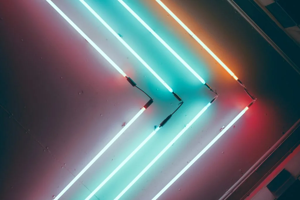 Cyan and orange neon tubes form nested chevrons on a dark wall.