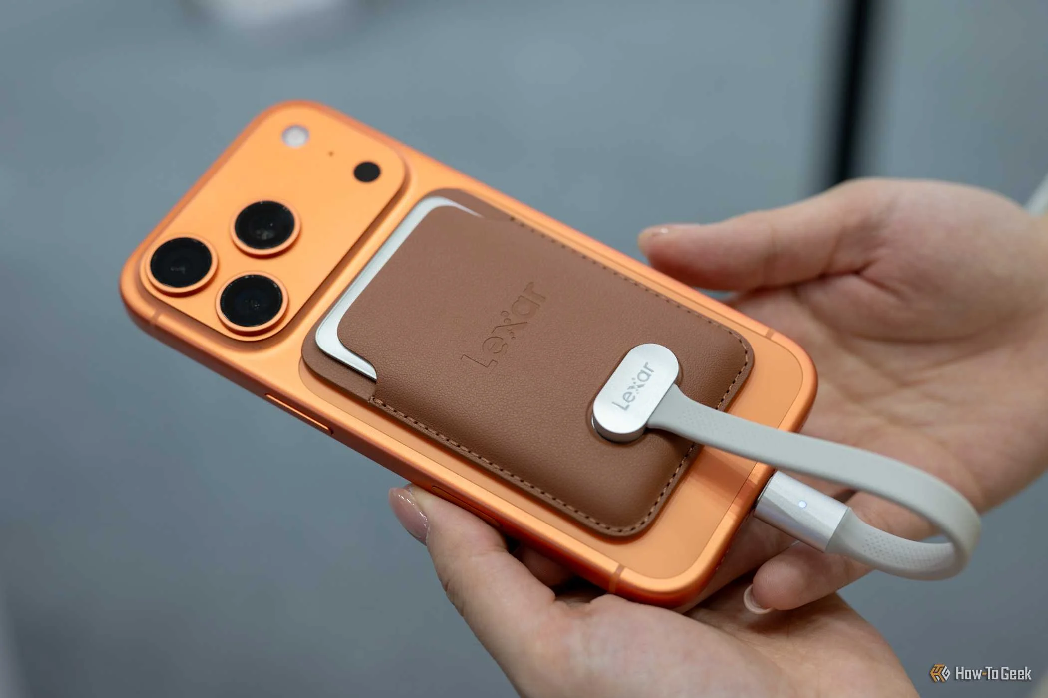 Person holding the Lexar Muse SSD in its MagSafe wallet connected to an iPhone at IFA 2026.