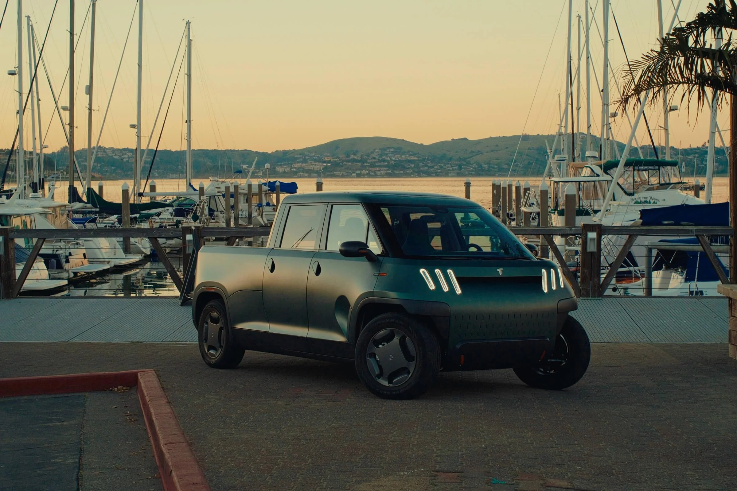 A small truck parked in front of a harbor at dusk.