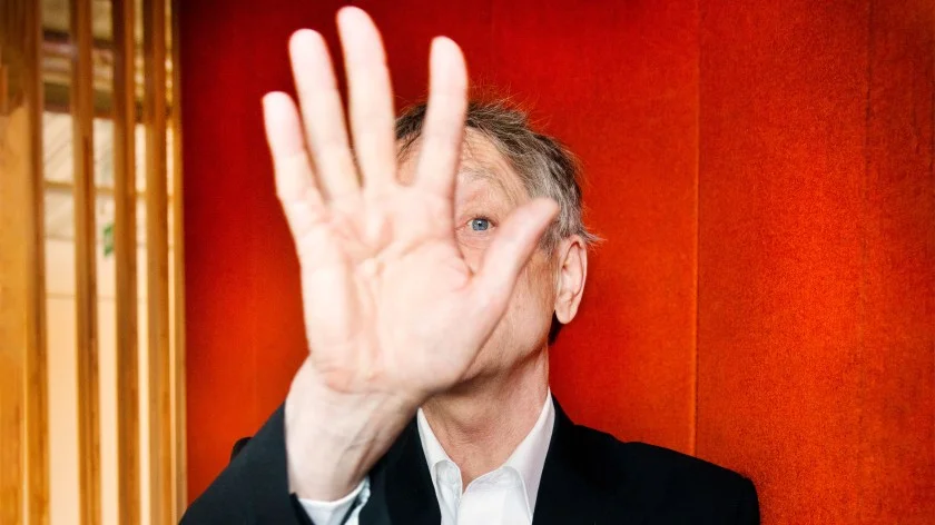 Geoffrey Hinton holds his hand up to partially obscure his face