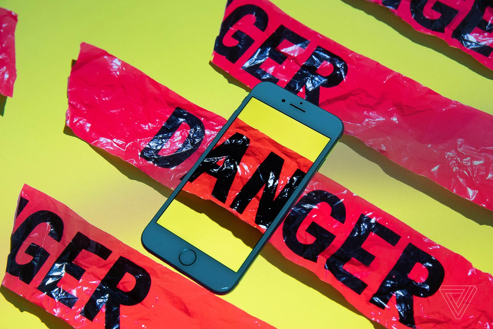 A smartphone sits on top of a surface with red tape reading “DANGER.” Where one strip intersects the phone, it continues inside the phone’s screen.